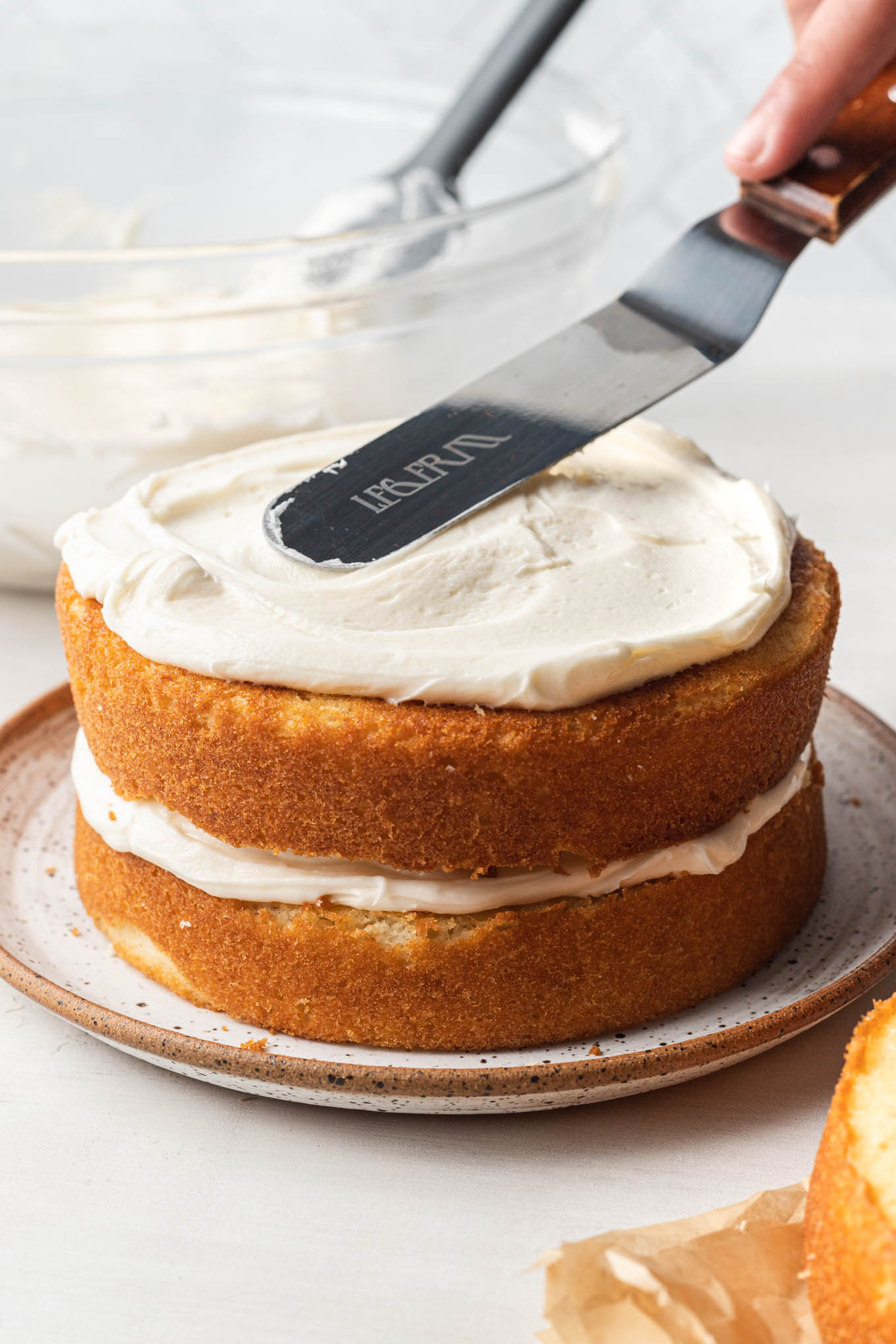 A 6-inch vanilla cake on a plate being assembled and frosted.