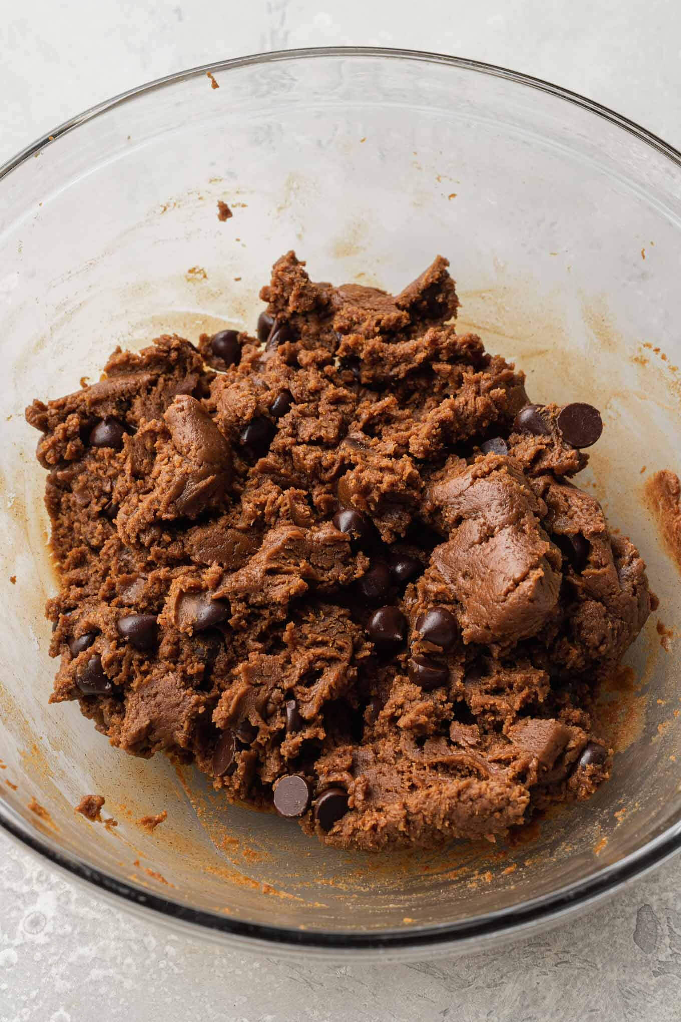 An overhead view of almond butter cookie dough with chocolate chips in a mixing bowl.