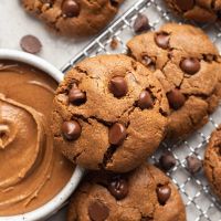 Several almond butter cookies on a wire rack. A bowl of almond butter is next to the cookies.