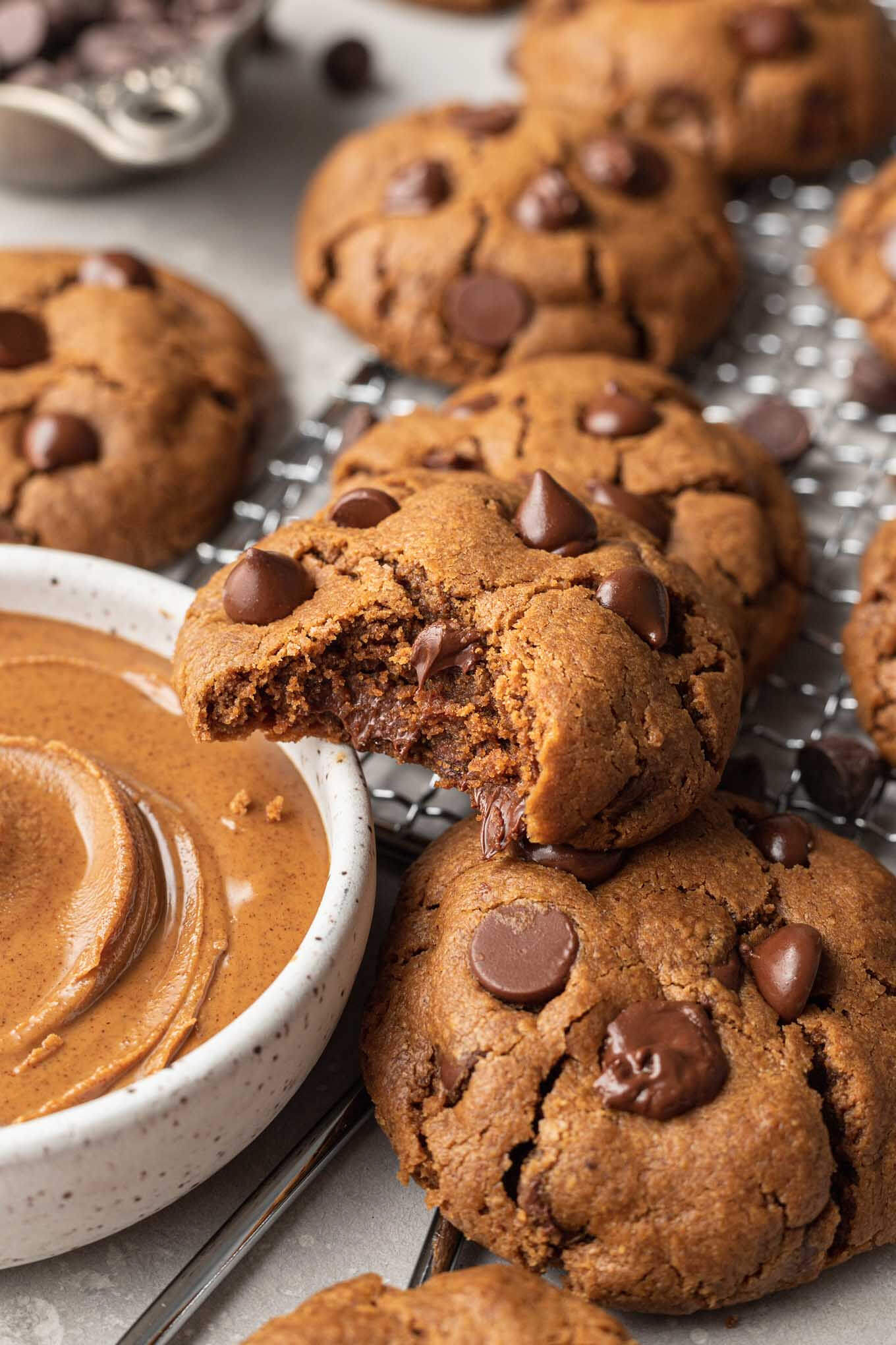 A close-up view of a cookie with a bite missing, resting on a dish of almond butter. 