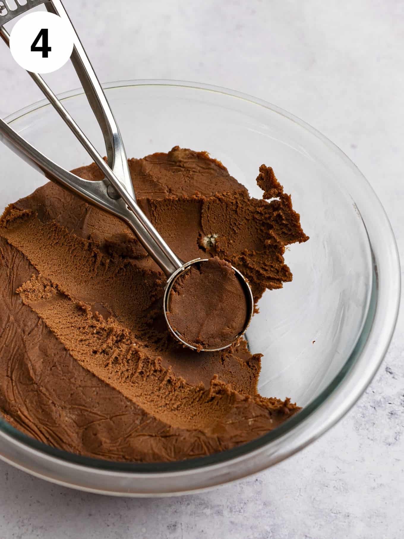 Chilled cookie dough in a glass mixing bowl with a cookie scoop.