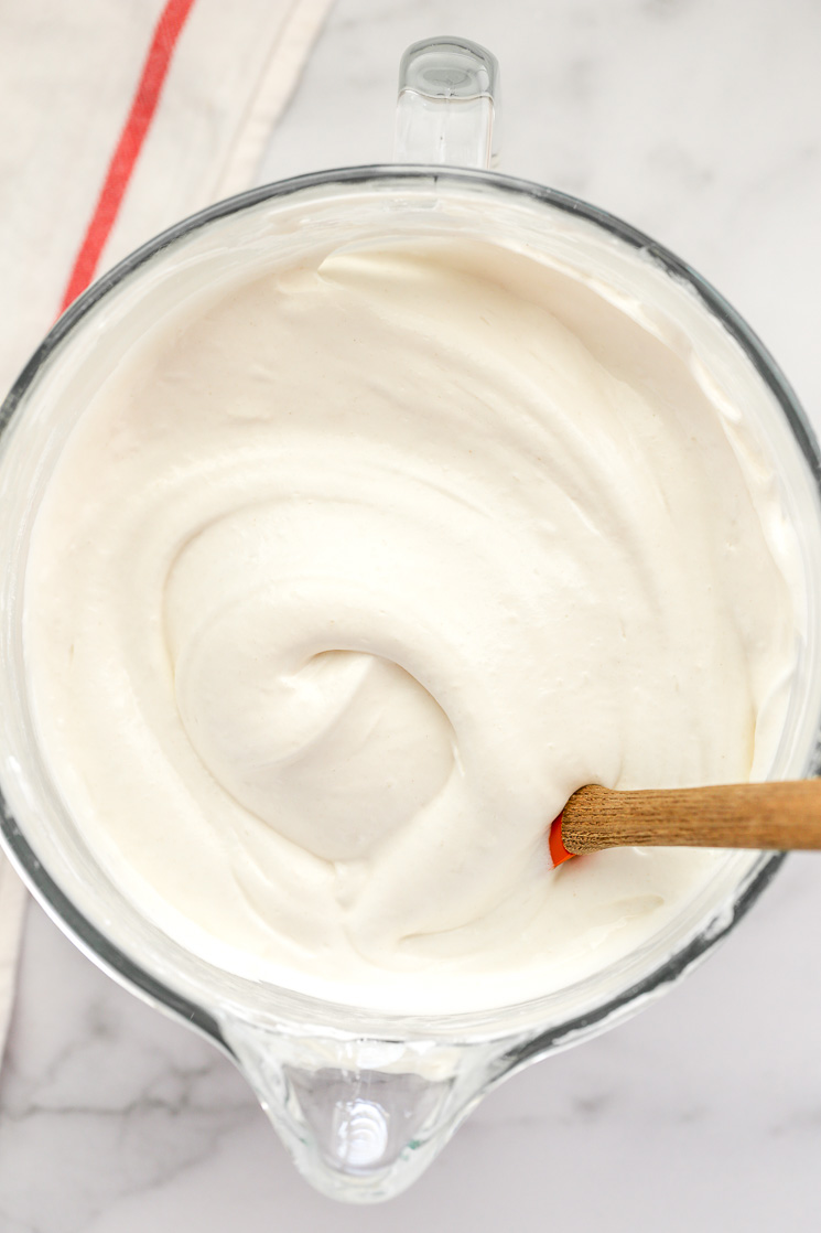 A glass bowl filled with angel food cake batter and a rubber spatula on the side.