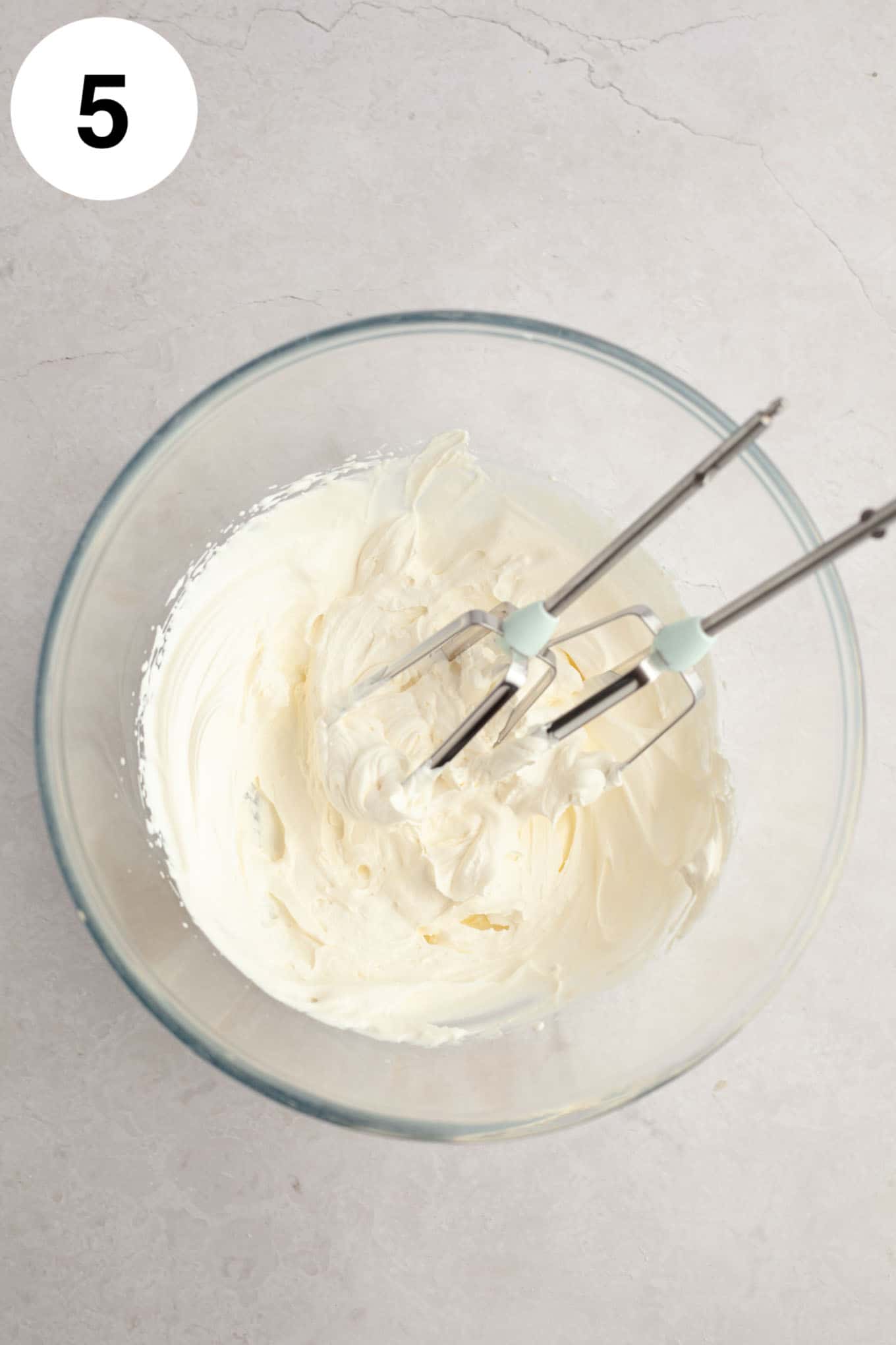 Whipped cream beat to stiff peaks in a glass mixing bowl.