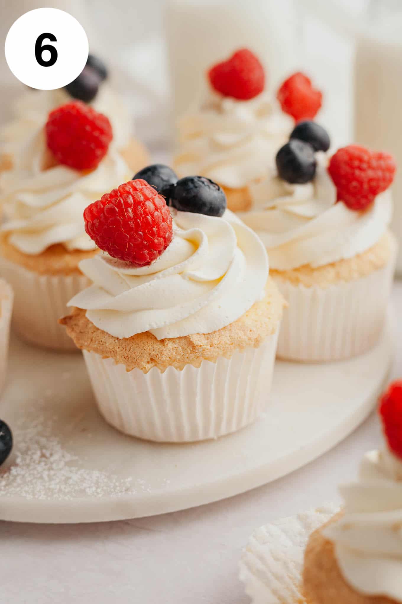 Several angel food cupcakes topped with whipped cream and fresh berries.