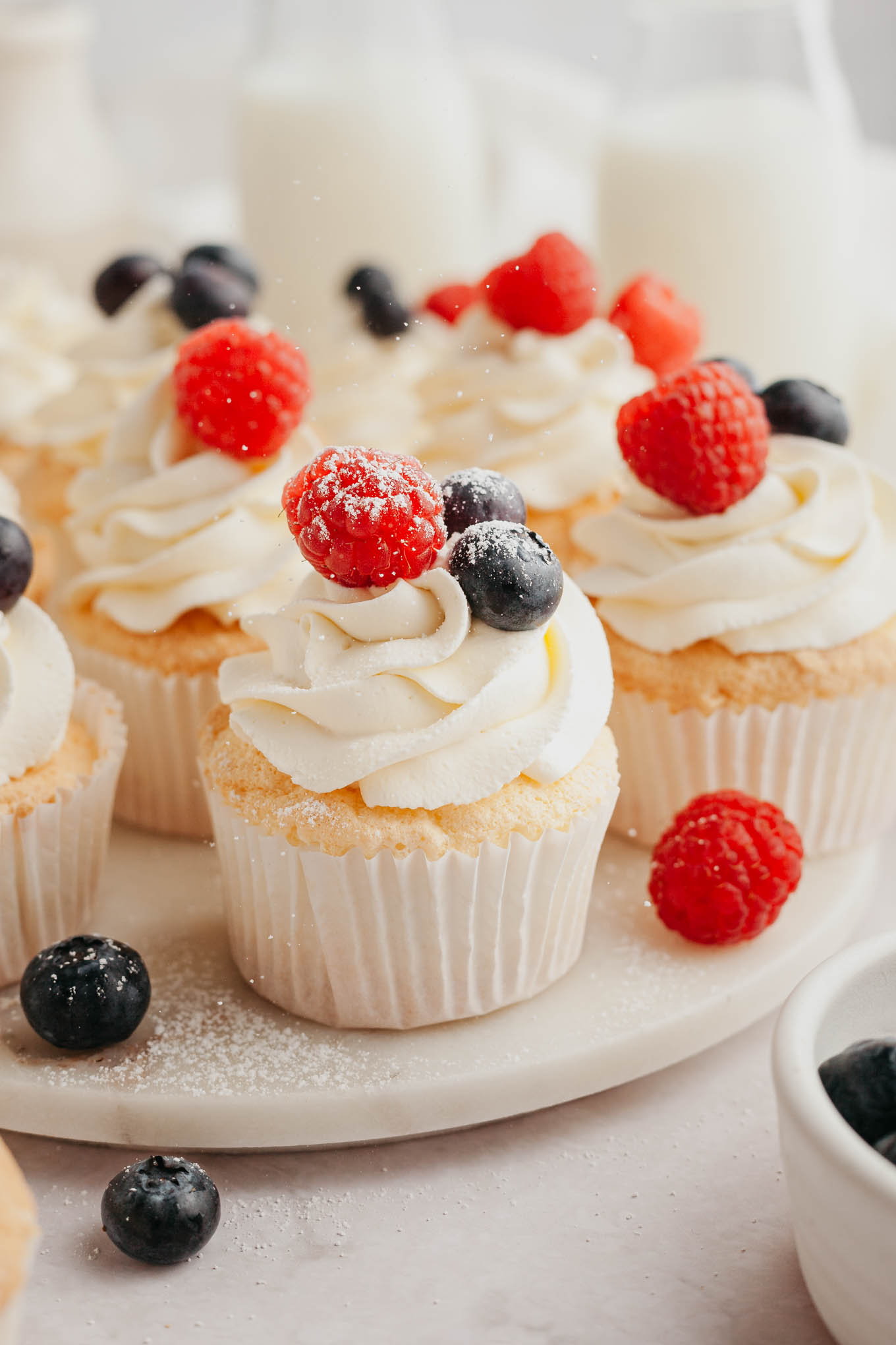 Angel food cupcakes topped with whipped cream on a serving plate. 