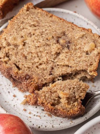 A slice of apple bread on a white speckled plate.