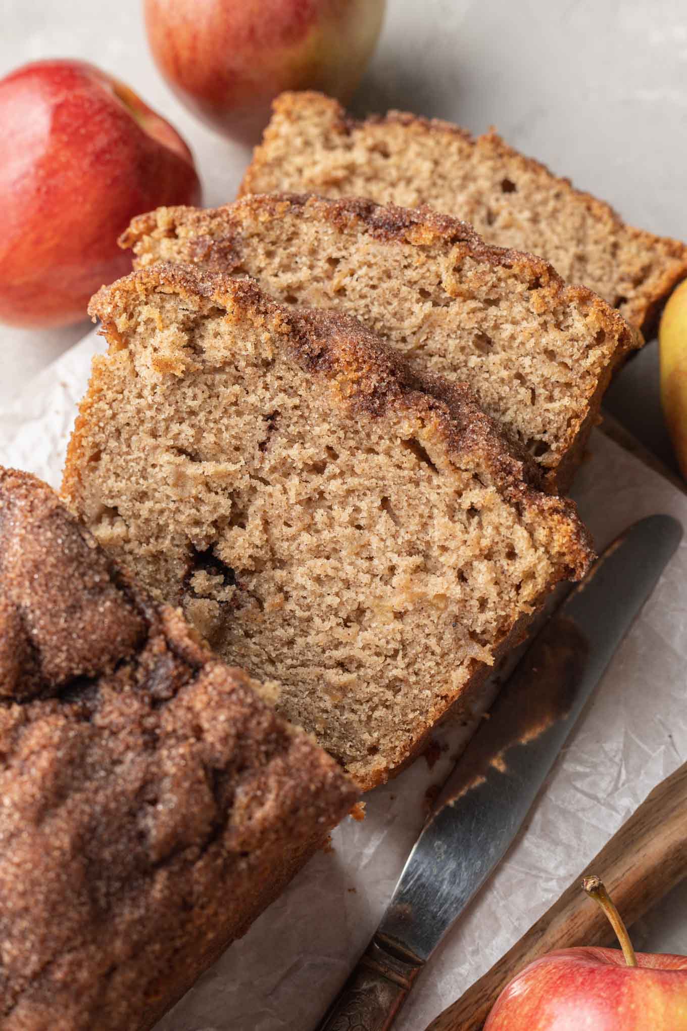 Three slices of apple bread, surrounded by apples. 