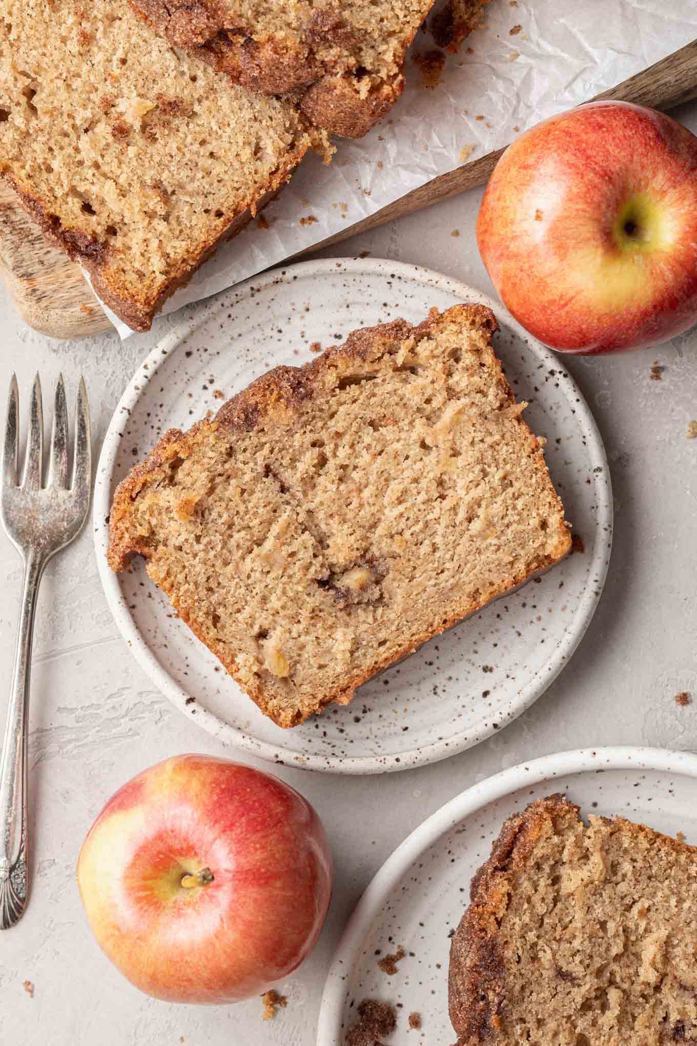 An overhead view of a slice of spiced apple bread on a dessert plate. Additional slices surround the plate. 