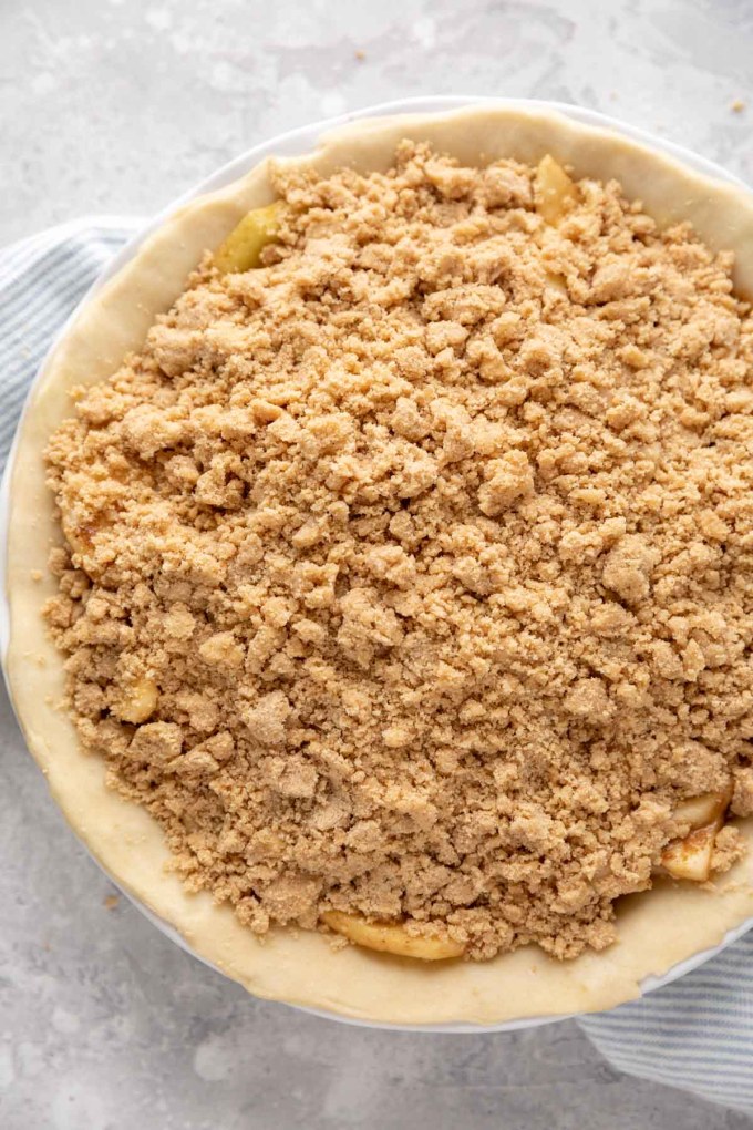 An unbaked apple crumble pie that's been topped with the crumb topping and is ready to go into the oven.