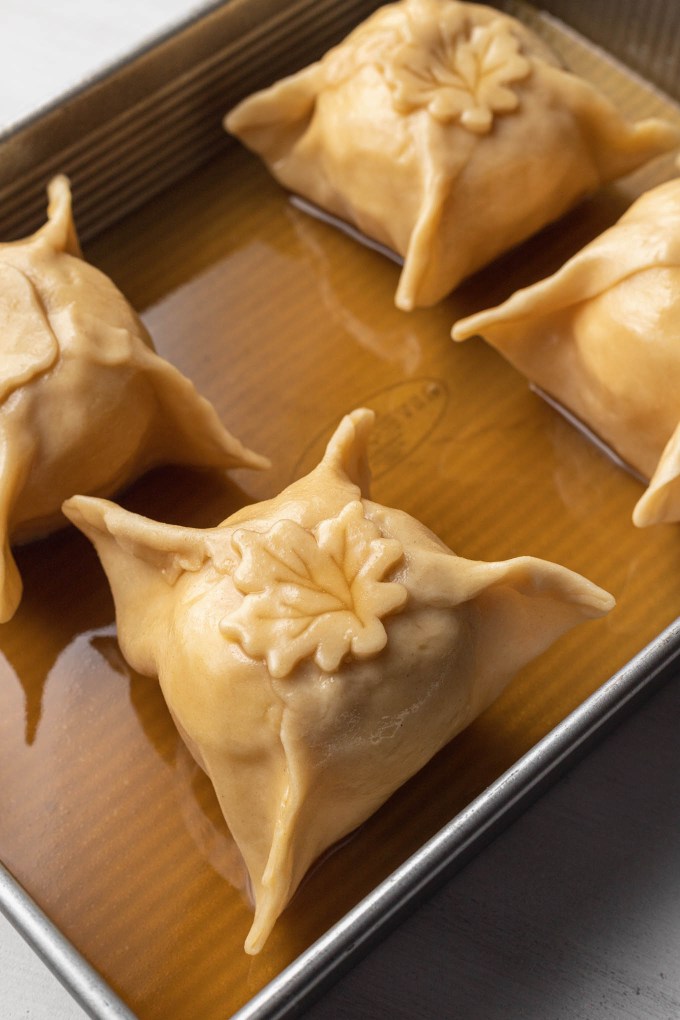 Unbaked apple dumplings with sauce in a baking tray.