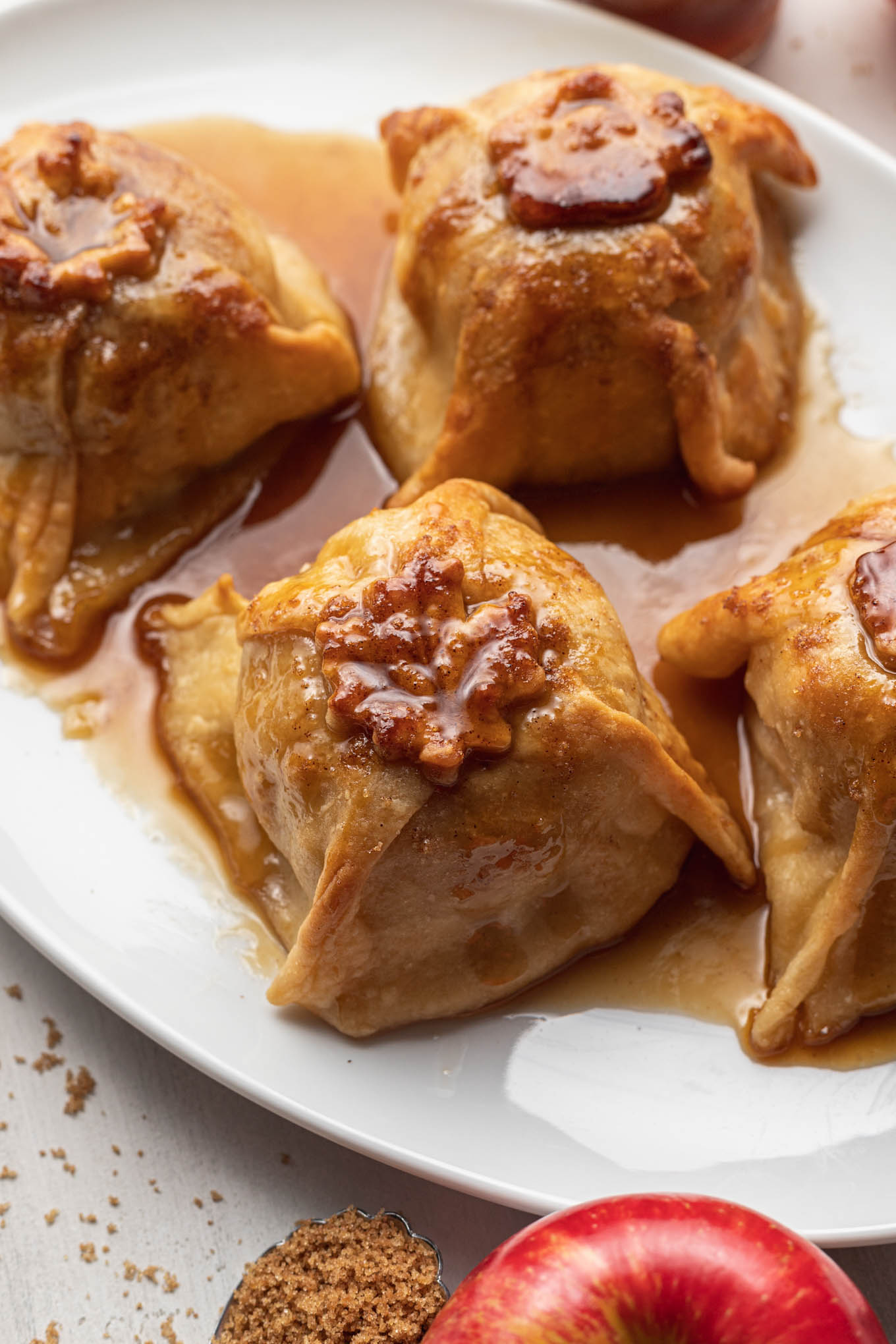 Four homemade apple dumplings with sauce on a white platter. 