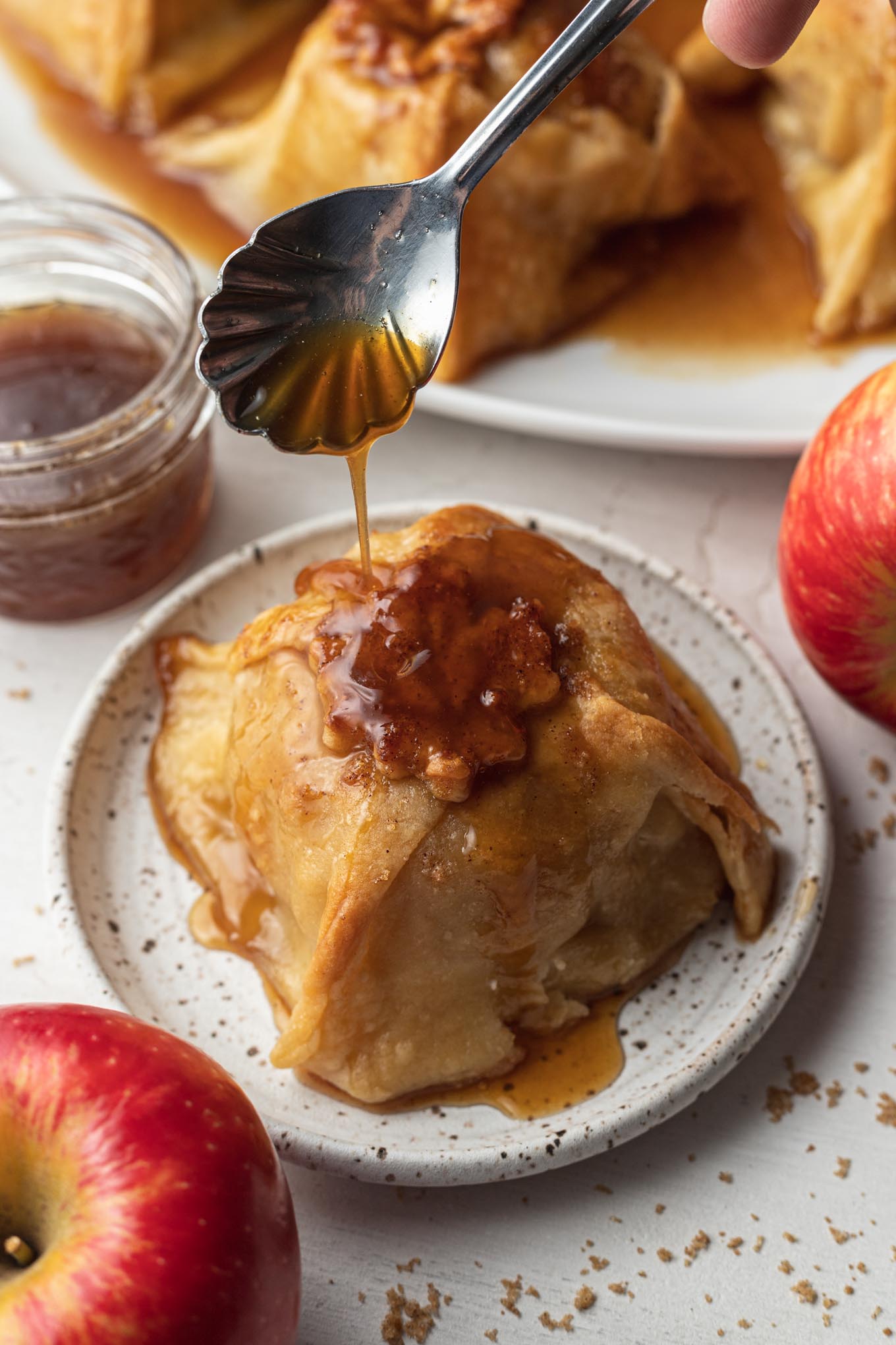 Sauce being spooned over a baked apple dumpling on a dessert plate. 