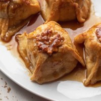 Four baked apple dumplings on a large white plate. The dumplings have been drizzled with extra sauce from the pan.