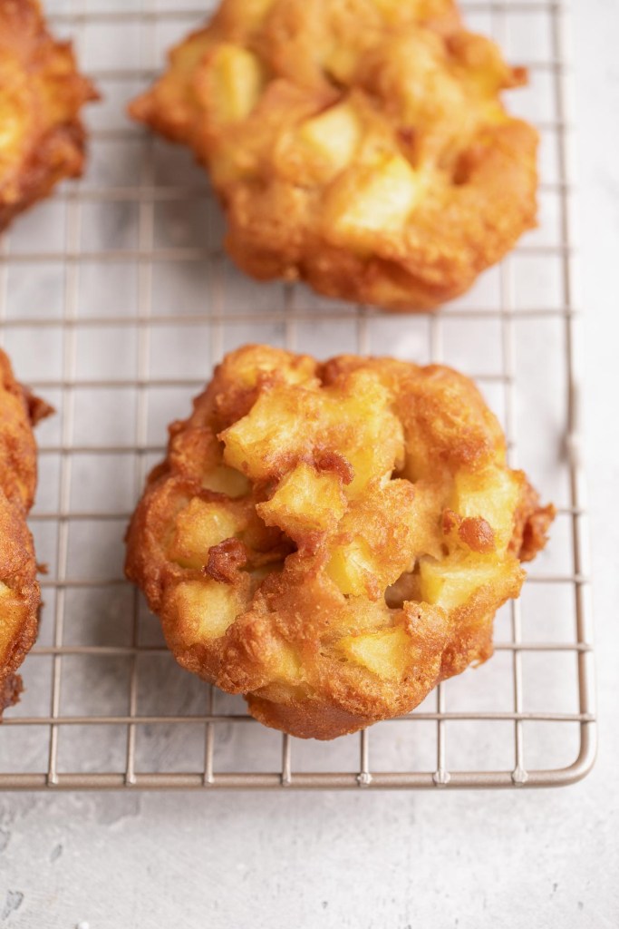 Homemade apple fritters cooling on a wire rack.