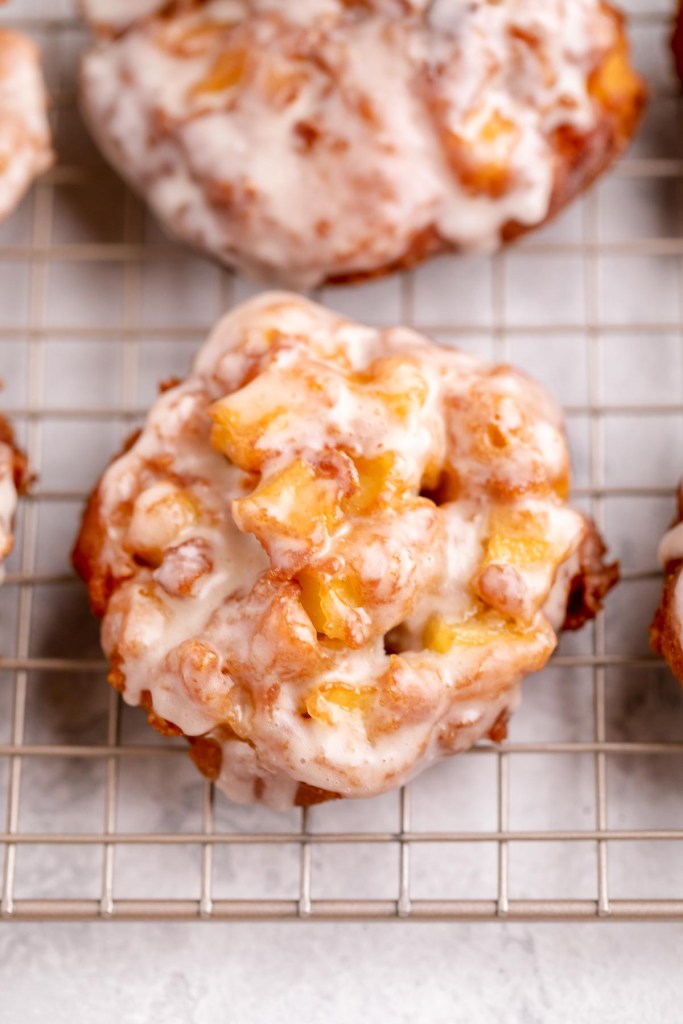 A cooling rack with several glazed apple fritters sitting on top of it.