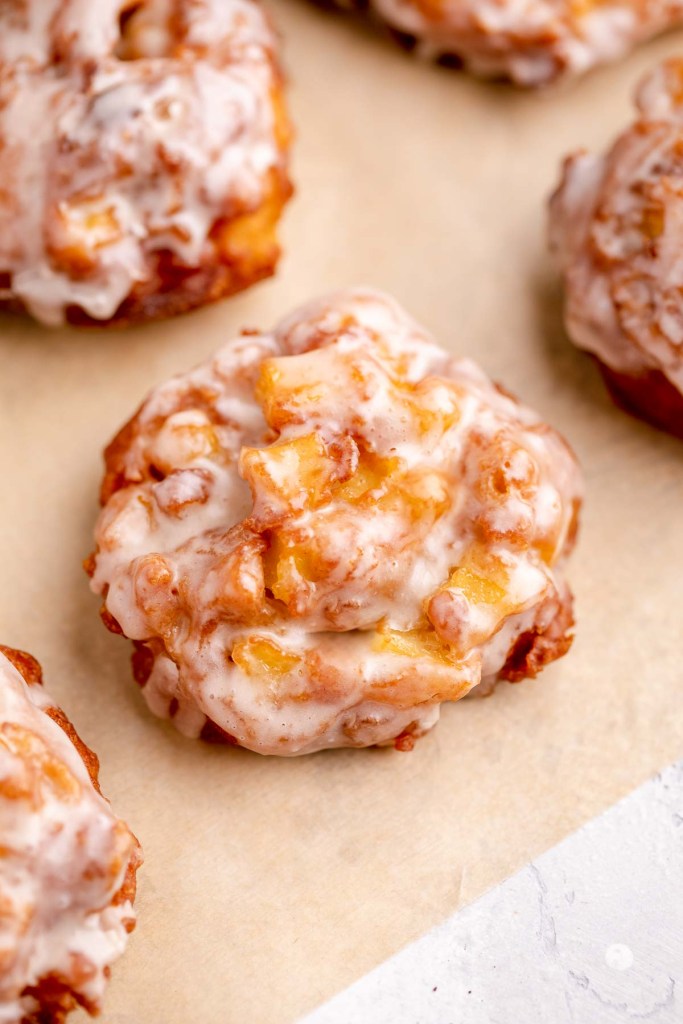 Glazed apple fritters on parchment paper. 