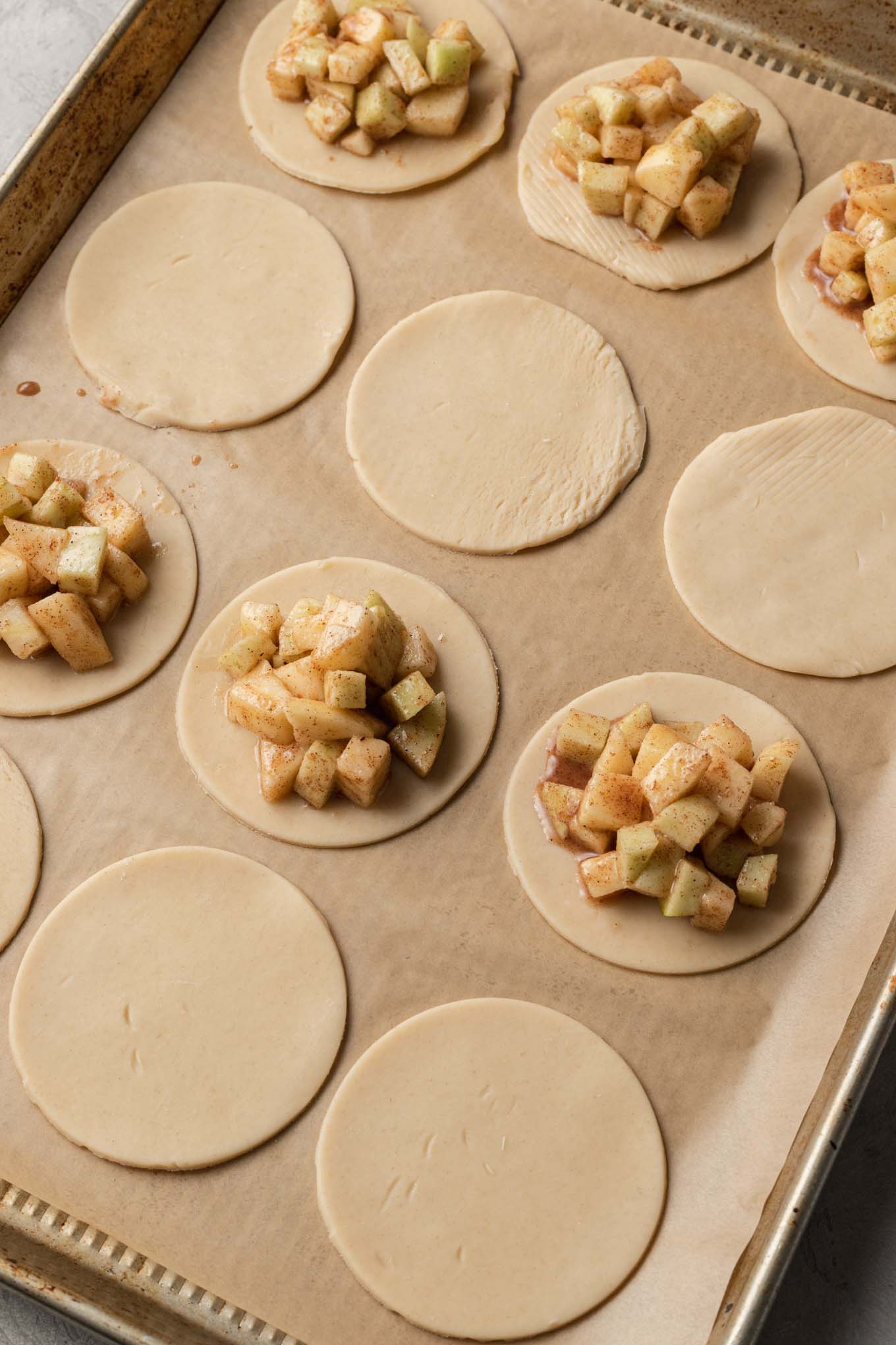 A process shot showing circles of pie dough filled with apple pie filling. 