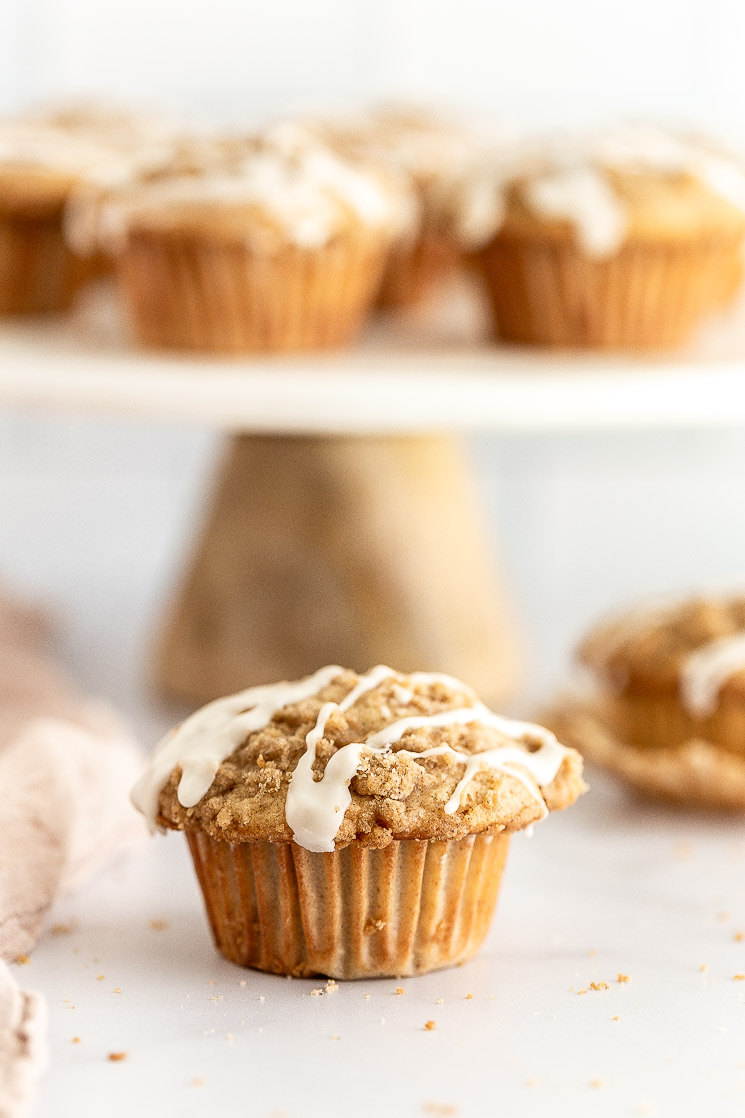 A close-up of an apple muffin with more muffins on a cake stand behind it.