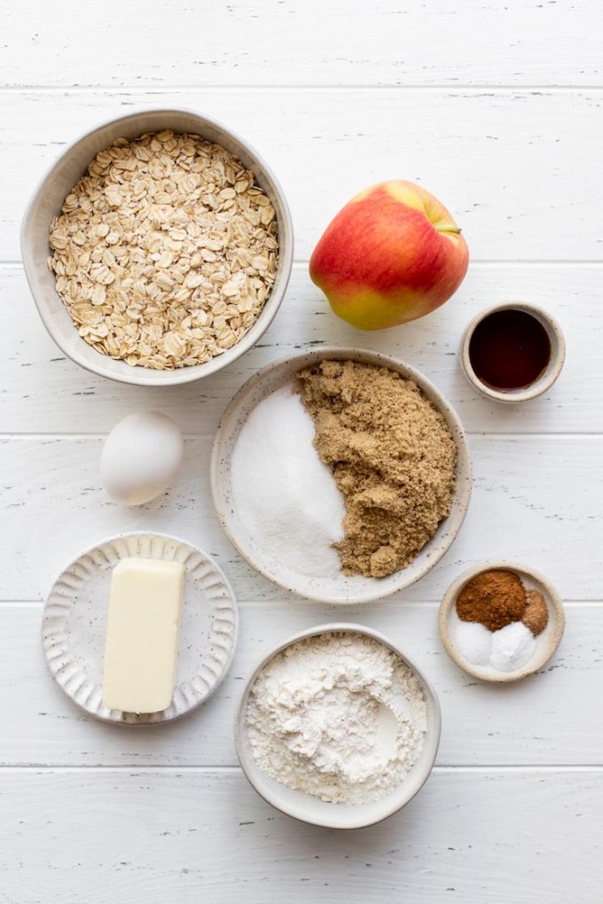 The ingredients needed to make apple oatmeal cookies laid out on a rustic white surface.