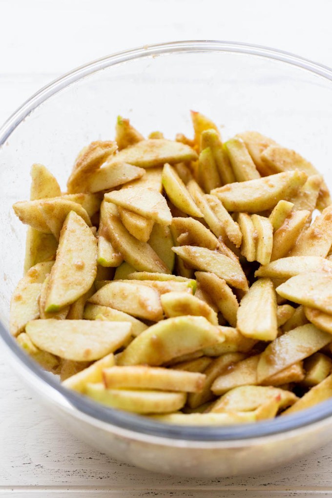 A glass mixing bowl holding sliced apples that have been coated in spices.