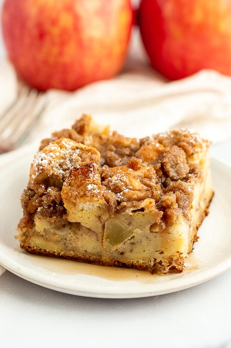 A slice of apple french toast casserole topped with maple syrup on a white plate.