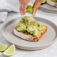 A slice of bread topped with avocado chicken salad. Fresh lime juice is being squeezed on top of it.