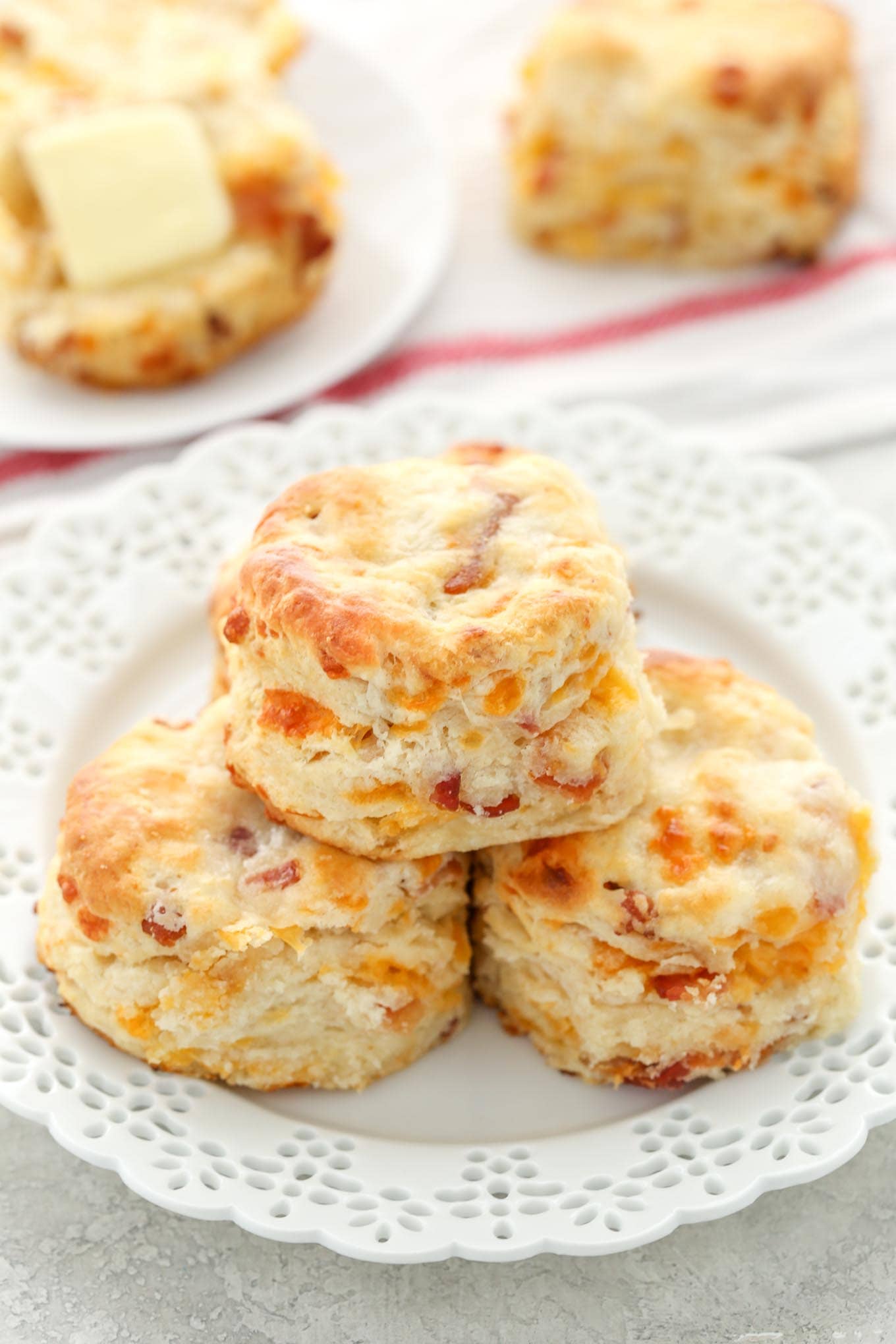 A stack of three bacon cheddar biscuits on a white plate. Additional biscuits rest in the background.