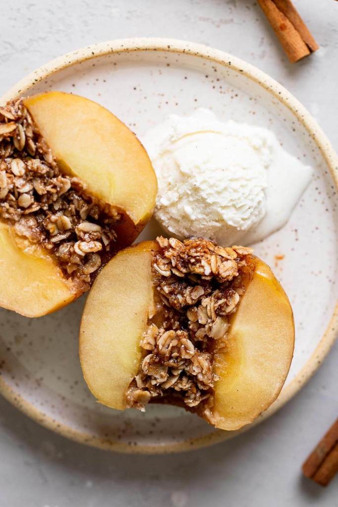 An overhead view of a baked apple that's been cut in half to show the oat filling. A scoop of ice cream is also on the speckled plate. 