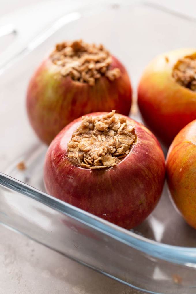 Whole apples in a glass baking dish that have been stuffed with a cinnamon oat mixture.