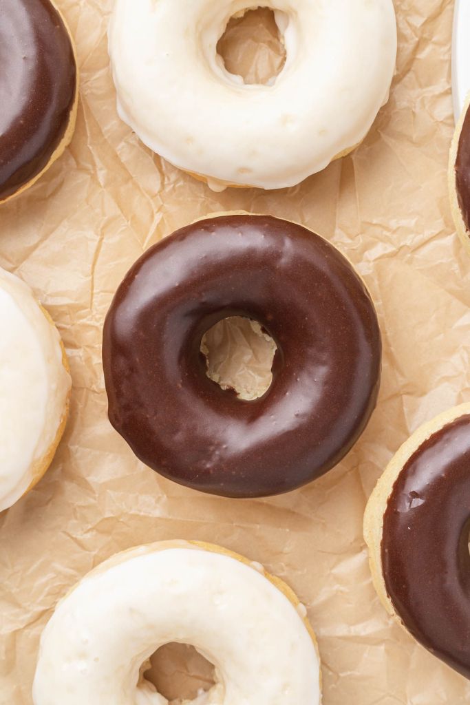 An overhead view of baked donuts with icing on a piece of parchment paper. 