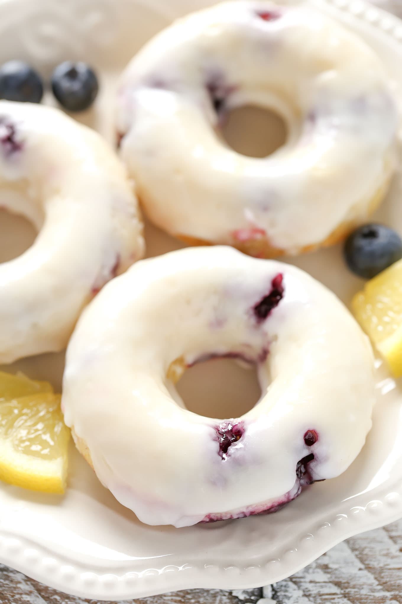 Three lemon blueberry donuts topped with glaze on a white plate. 