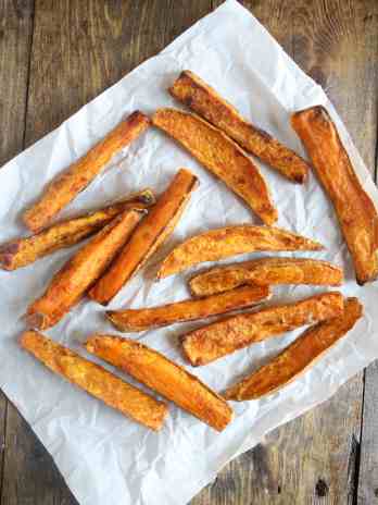 Overhead view of oven baked sweet potato fries on a square of parchment paper.