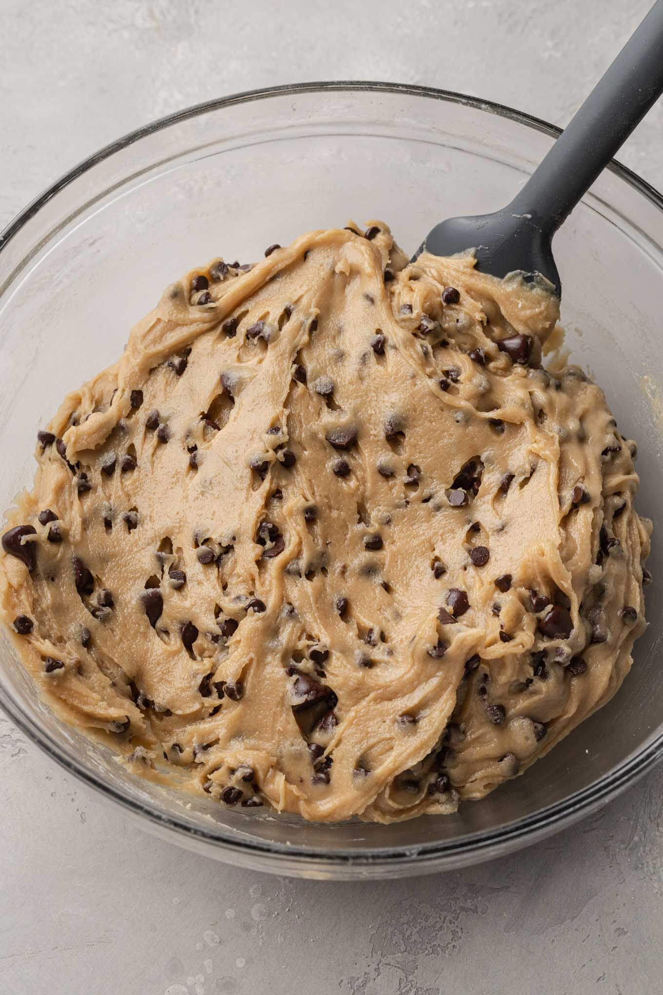 A glass mixing bowl filled with the finished chocolate chip cookie dough.