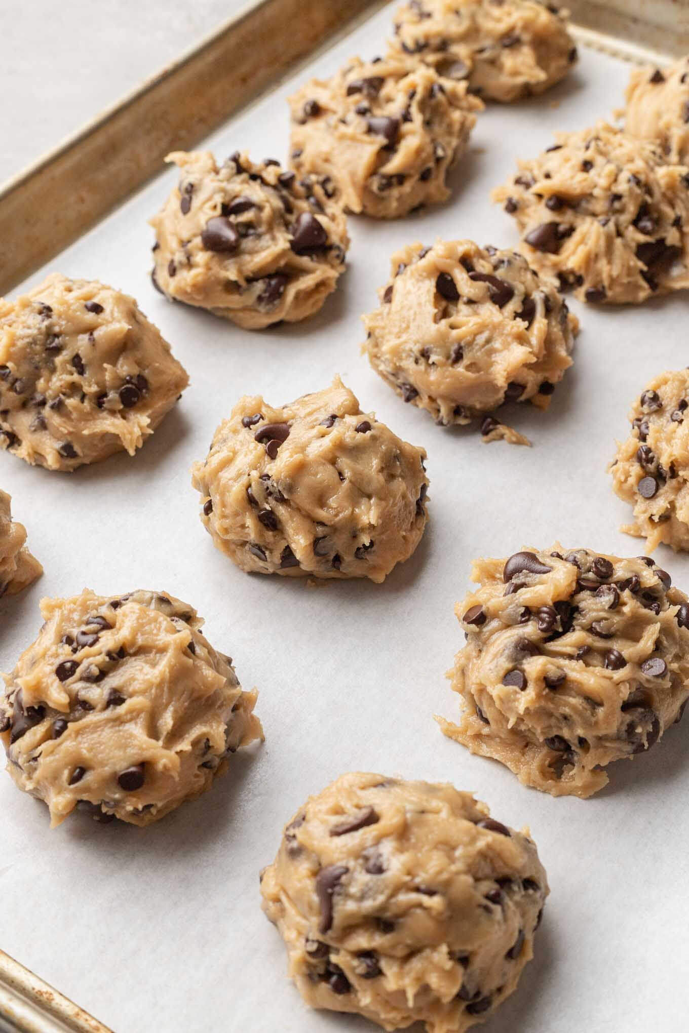 A baking sheet lined with parchment paper with balls of cookie dough scooped on top.