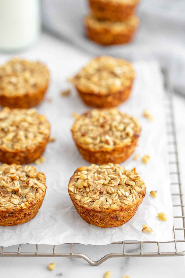 A cooling rack lined with parchment paper with multiple banana baked oatmeal cups on top.