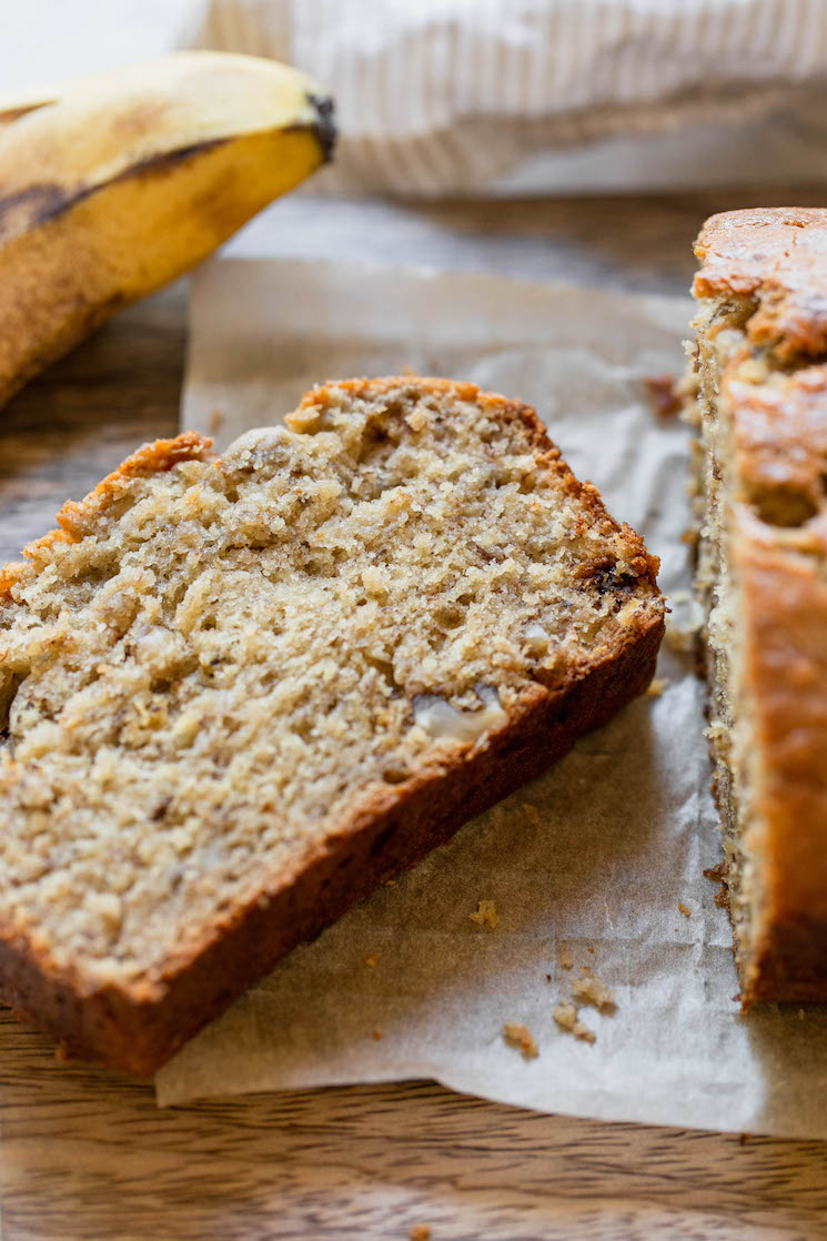 A slice of banana bread cut off the loaf and laying down to show the crust and interior texture of the bread.