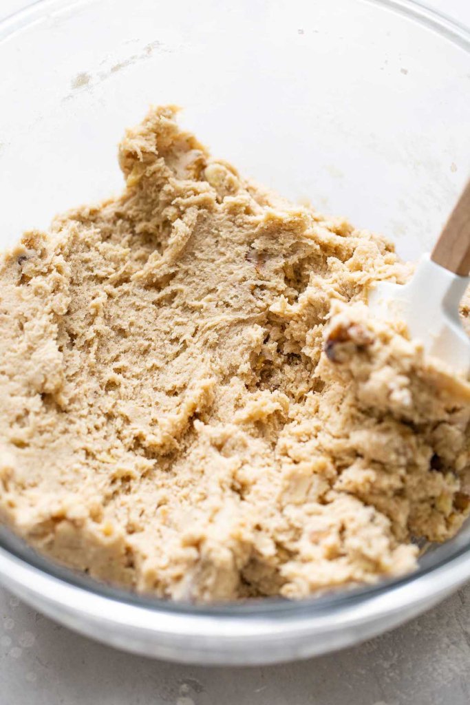 Banana nut cookie dough in a glass mixing bowl with a rubber spatula. 