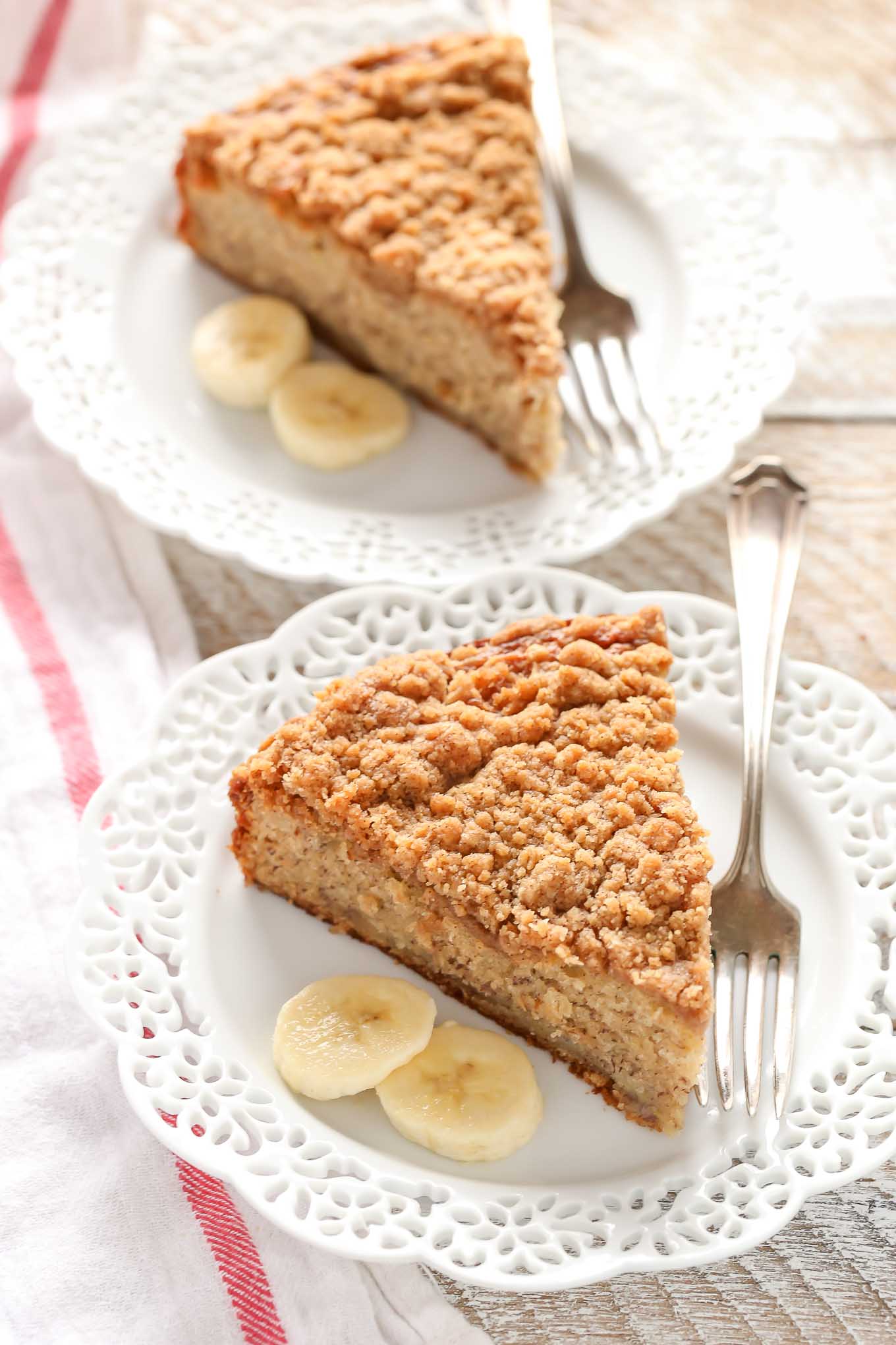 Two slices of banana cake with buttermilk on white plates. Forks and banana slices are also on the plates. 