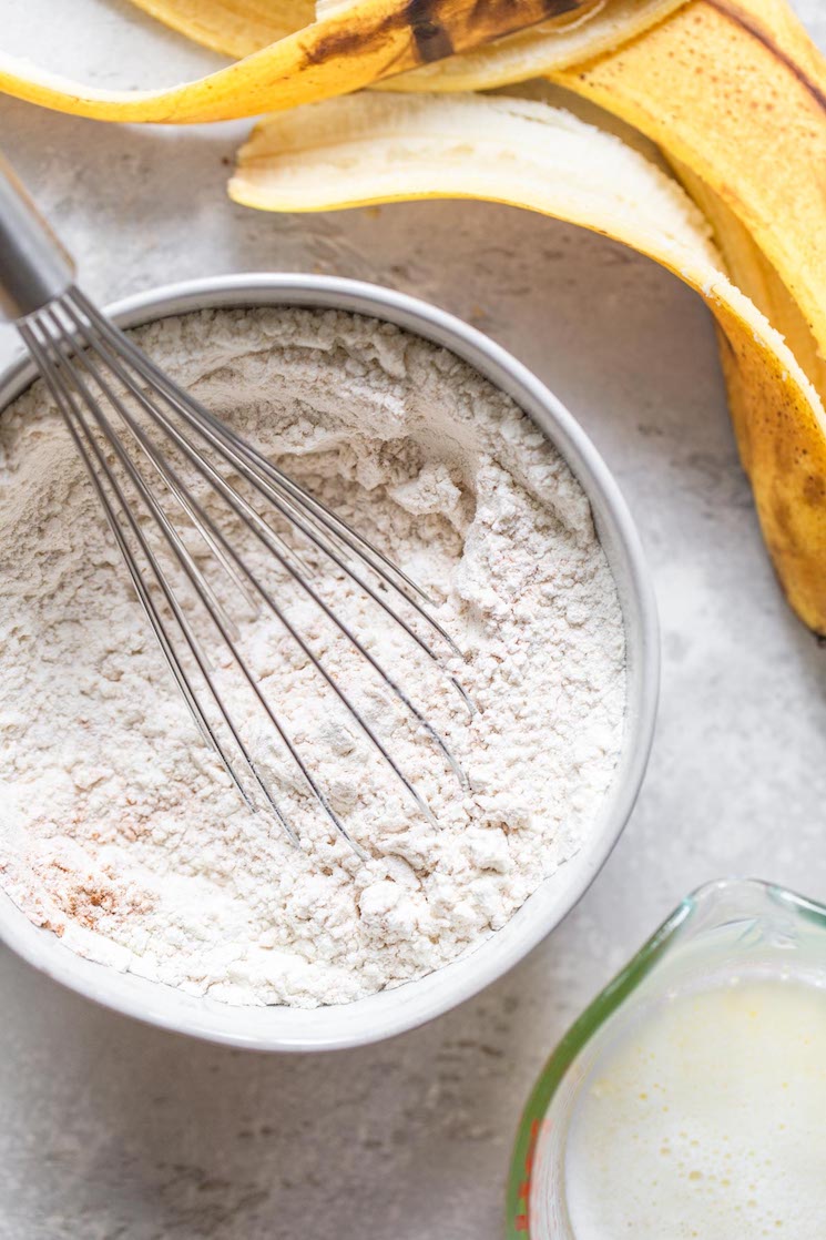 A white bowl with the dry ingredients whisked together and a banana peel and milk in the background.