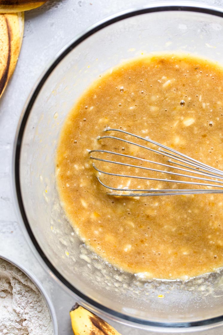 A glass bowl with the wet ingredients whisked together on a distressed gray surface.