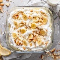 Overhead view of a baking dish filled with banana pudding from scratch. Crushed Nilla Wafers and a banana peel surround the baking dish.