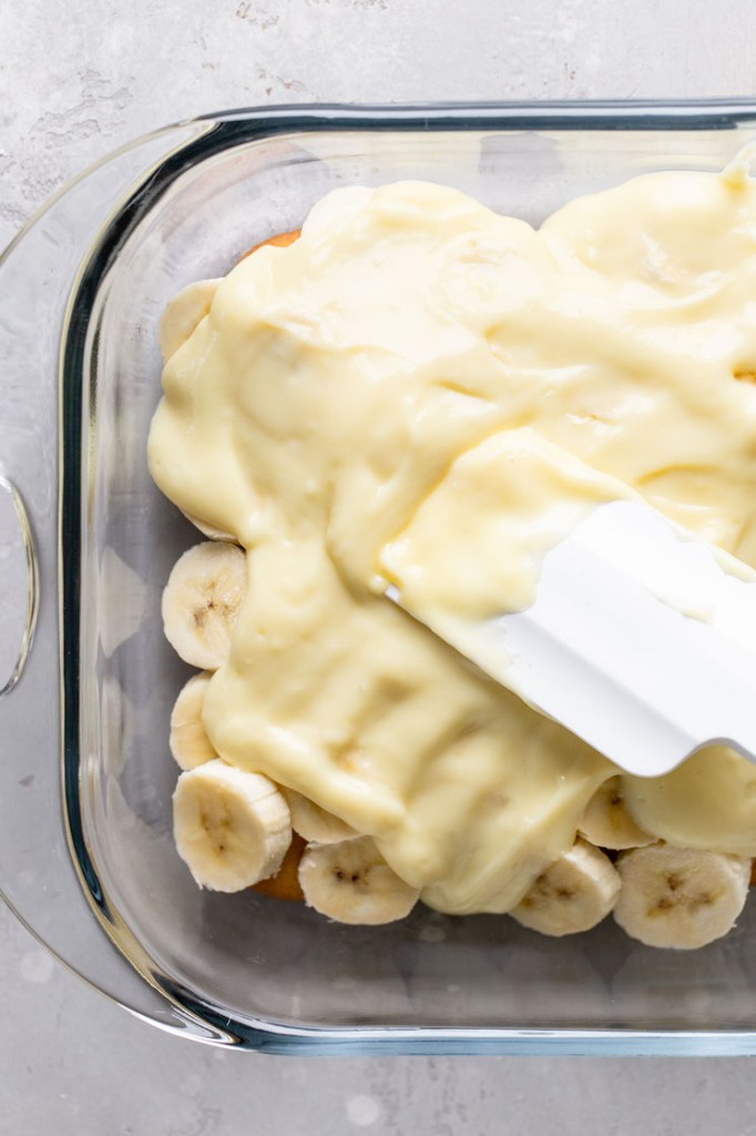 Overhead view of homemade vanilla pudding being spread over a layer of Nilla Wafers and banana slices. 