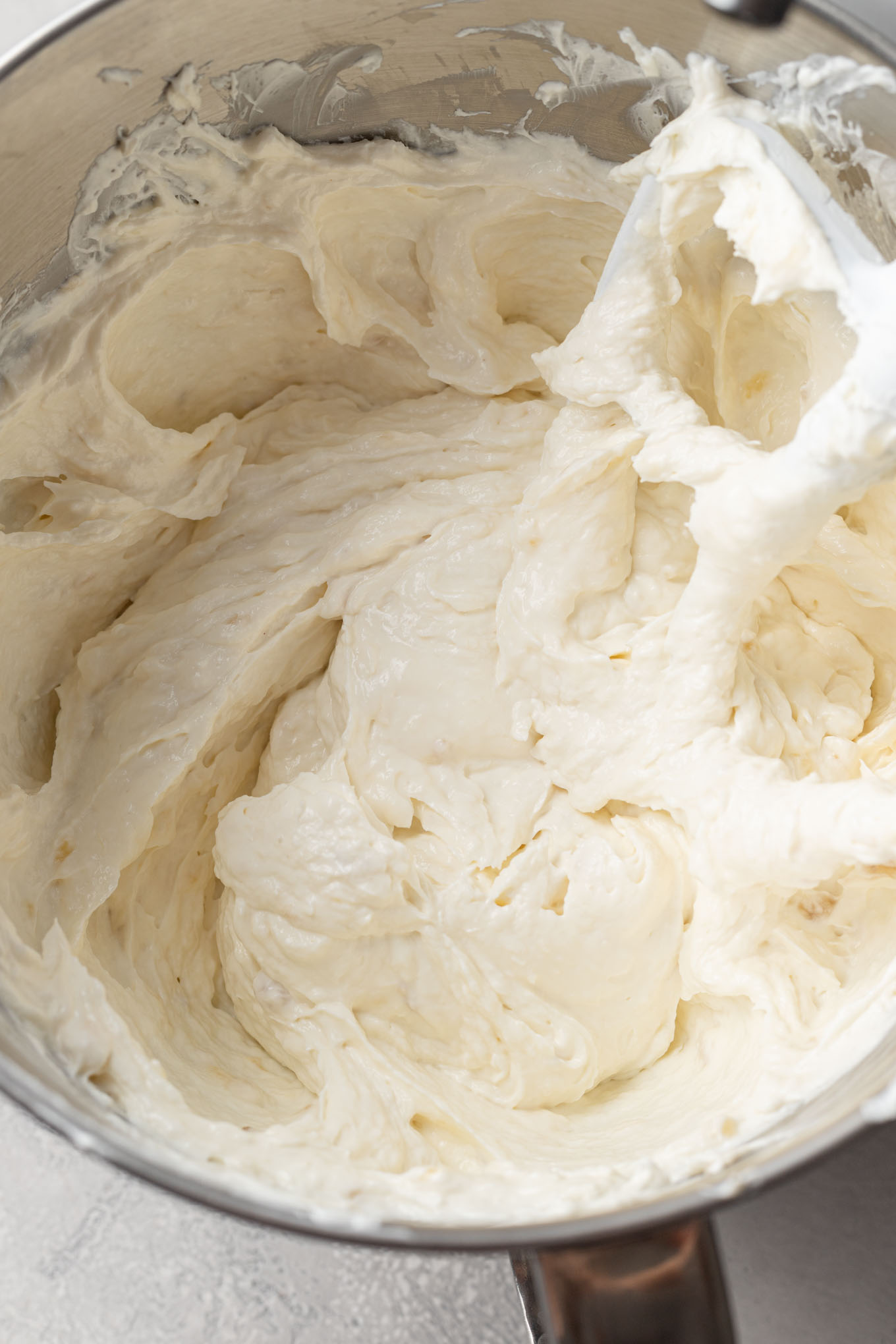 Beaten cream cheese, sour cream, and bananas in a mixing bowl with a paddle attachment.