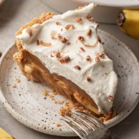 A slice of banoffee pie on a speckled white plate with a fork resting on the side.