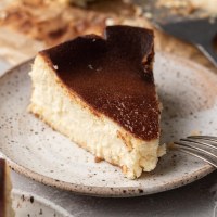 A slice of basque cheesecake on a white speckled plate. A fork is resting on the plate.