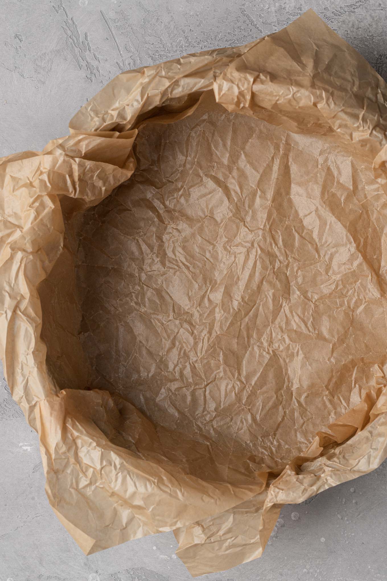 A springform pan lined with two overlapping pieces of parchment paper.