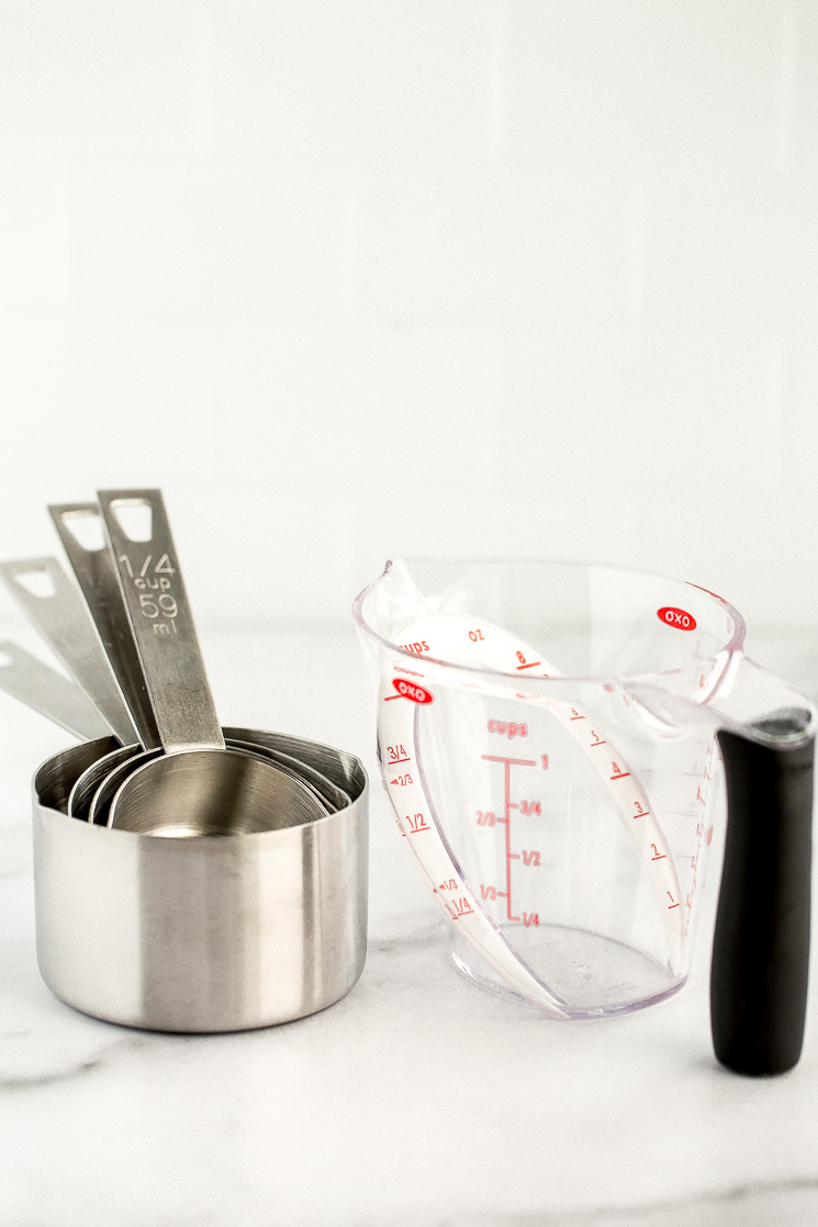 A set of metal measuring cups and a plastic angled liquid measuring cup sitting on a marble counter.