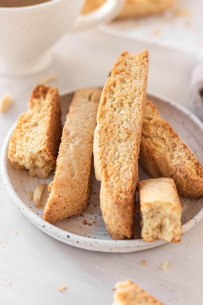 Almond biscotti on a white speckled plate. One cookie has been broken into pieces. 