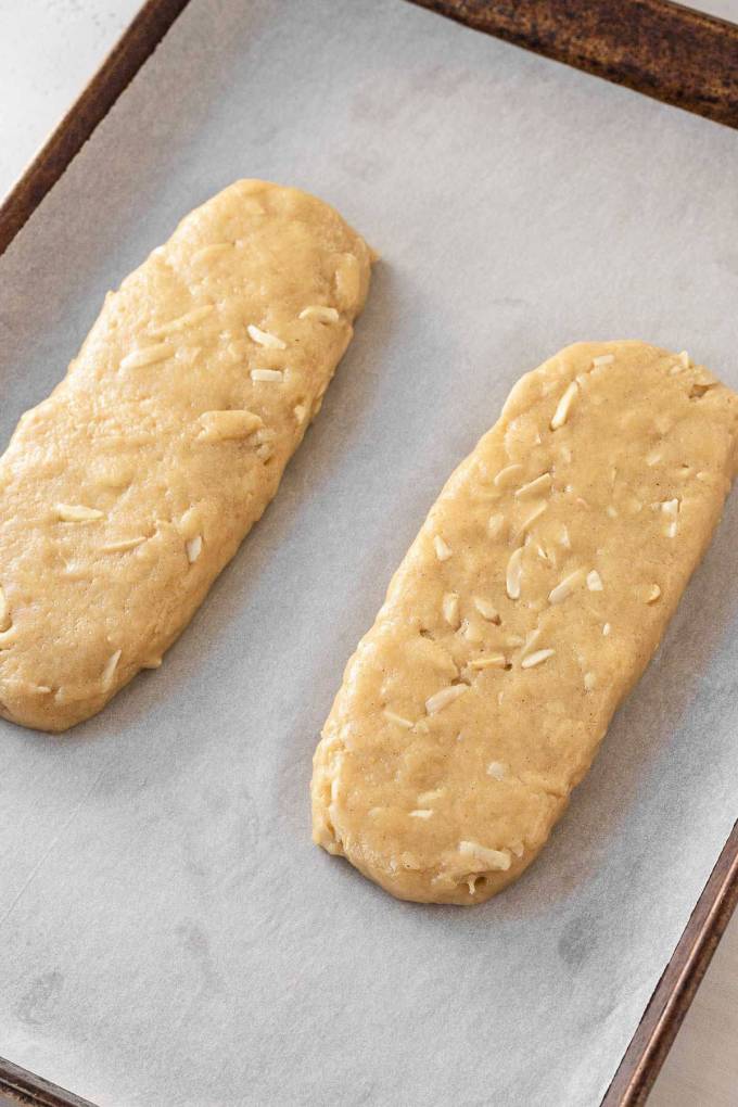 Two unbaked logs of biscotti dough on a parchment paper-lined baking sheet.