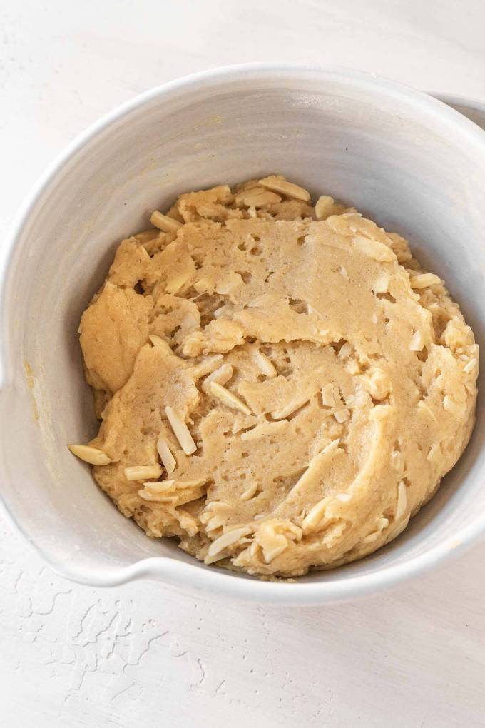 An overhead view of a white mixing bowl full of almond biscotti dough.